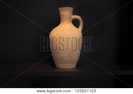 Terracotta caraffe earthenware household item with handle handmade on a dark shelf isolated on black.