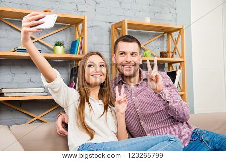 Cute Couple Making Photo On Smartphone And Showing Two Fingers