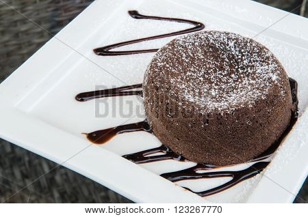 Chocolate lava cake topped with chocolate cream on a white plate.