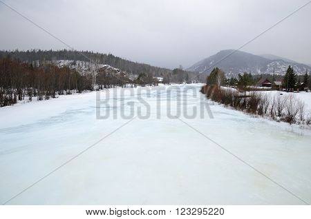 Icebound river on a cloudy spring day in the village. Kochergat Irkutsk Region Russia