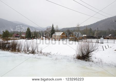 Icebound river on a cloudy spring day in the village. Kochergat Irkutsk Region Russia