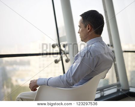 caucasian business executive sitting by the window in a chair thinking in office.