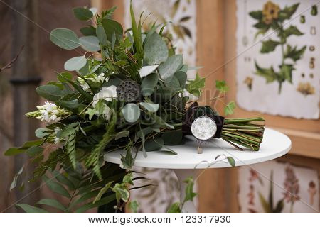 Green wedding bouquet of eucalyptus ivy fern aspidistra ruskus date fruit pink ranunkulyus with flax box green and brown velvet ribbons on white stand and brown and green floral pattern on background