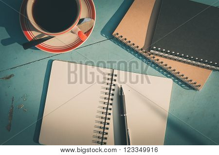 Morning scene of small notebook and pen beside coffee cup on blue wood table at outdoor area in cafe with vintage filter effect