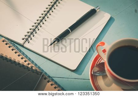 Small notebook and pen beside coffee cup on blue wood table at outdoor area in cafe with morning scene and vintage filter effect