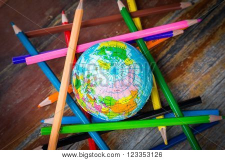 Photo of world and color pencil together on wooden surface