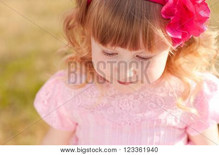 Cute baby girl 3-4 year old with pink flower in blonde hair outdoors. Looking down. Top view. Childhood.