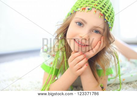 Cute girl wearing a green hat on a furry white carpet