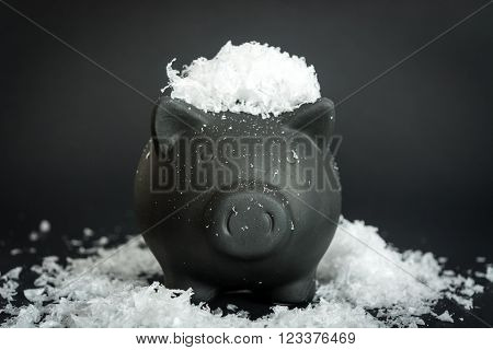 Black piggy bank on the snow-covered table and snow on the head of a pig