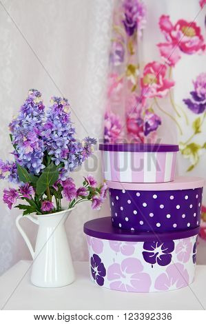 Bouquet branches purple lilac in a white vase on a table and a set of gift boxes in room