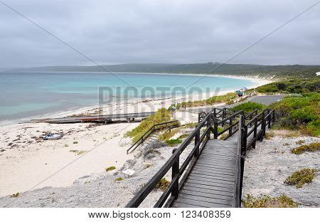 Turquoise Indian Ocean seascape from elevated boardwalk on the limestone cliffs at at Hamelin Bay beach under dark, stormy skies  with boat ramp and vegetated dunes in Western Australia.