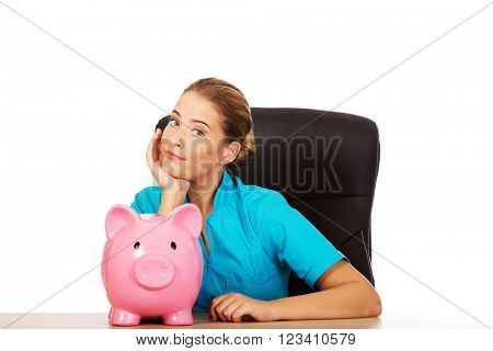Young female doctor or nurse holding piggybank