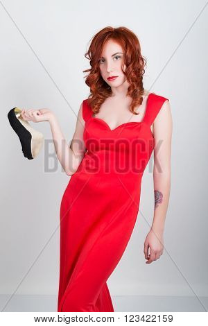 Beautiful young sexy slim red-haired girl wearing a silk red dress high heels, in alcoholic intoxication. drinking red wine from a glass. after party.