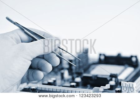 Hand with tweezers above board with components. Repair of computers and modern technologies. PCB.