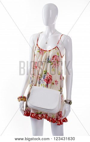 White leather purse on mannequin. Female mannequin wearing simple handbag. Floral sarafan and white bag. Summer clothing with wrist accessories.