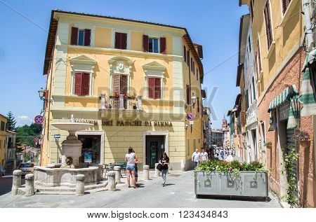 Asciano, Italy, May 31, 2015 - People walk and chat in the small square with fountain