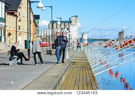 Ahus Sweden - March 20 2016: People outside enjoying the fine weather and eating ice cream by the marina. Early spring before the tourist season starts. Real people in everyday life.