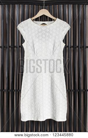 White lacy dress on clothes rack hanging on black rattan screen