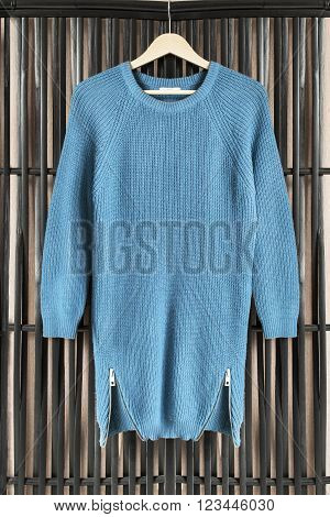 Blue knitted dress on clothes rack hanging on black bamboo screen