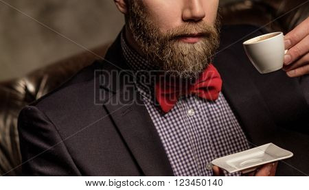 Old-fashioned bearded man sitting in comfortable leather sofa with cup of coffee 