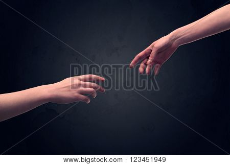 Two male hands reaching out to one another, almost touching, in front of dark clear empty background wall concept