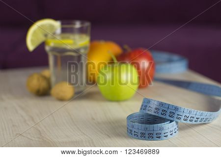 blue measure tape with diet food (color fresh fruits, nuts and lemon water in glass)