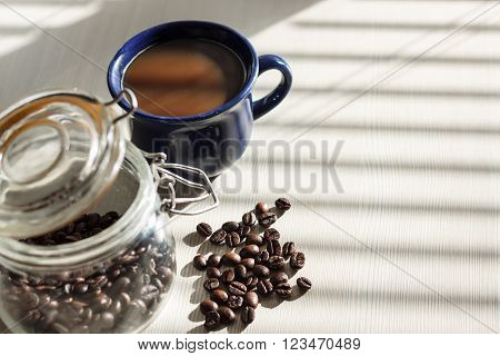 Black coffee in blue cup on white table with shadows from the blinds on sunny morning hotizonal view with copy space