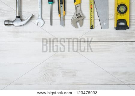 Top view of construction instruments and tools on wooden DIY workbench. Tape measure, wrench, hammer, pilers, screwdriver. Flat lay.