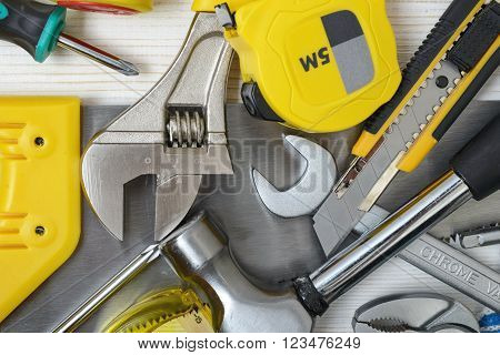 Top view of construction instruments and tools on wooden DIY workbench. Tape measure, saw, wrench, hammer, pilers, screwdriver. Flat lay.