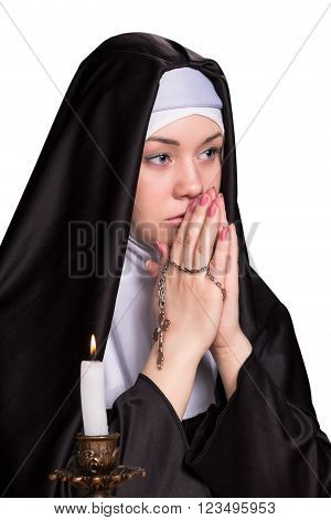 Portrait of nun with her hands folded together and holding a cross with candle burning near isolated on white background