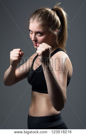 Girl with fists in rack. Young beautiful aggressive woman with fists in defense against dark background