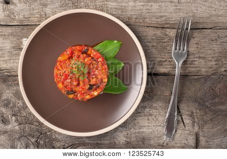 Vegetable stew in a brown plate on a wooden background, top view. Healthy food