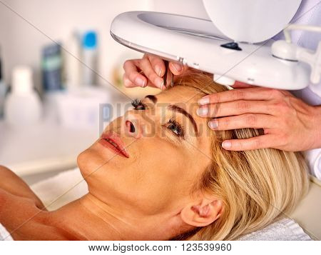 Woman middle-aged in spa salon with young beautician. Tweezing eyebrow by beautician. Aesthetic medicine.
