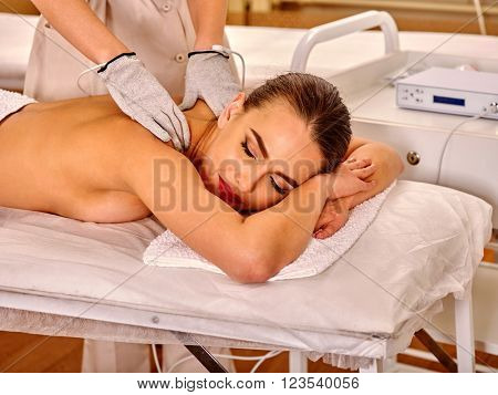 Woman  receiving electric back massage at beauty salon. Beautician wearing electricity gloves. In room is device for hardware cosmetology. Modern technologies in beauty.