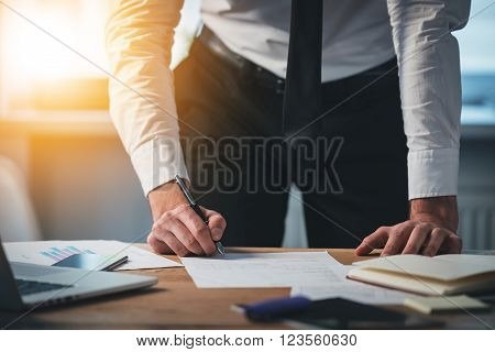Signing contracts on the go. Close-up part of young man signing documents while standing at his working place