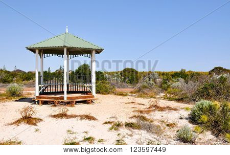 Wooden gazebo shelter set in green vegetated coastal dunes under a clear blue sky in Jurien Bay, Western Australia.