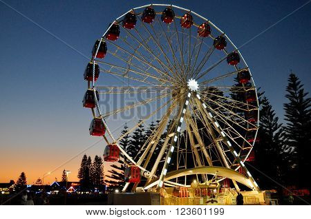 FREMANTLE,WA,AUSTRALIA-SEPTEMBER 30,2015: Ferris Wheel amusement ride lit up at twilight with red gondola's  and people in Fremantle, Western Australia.