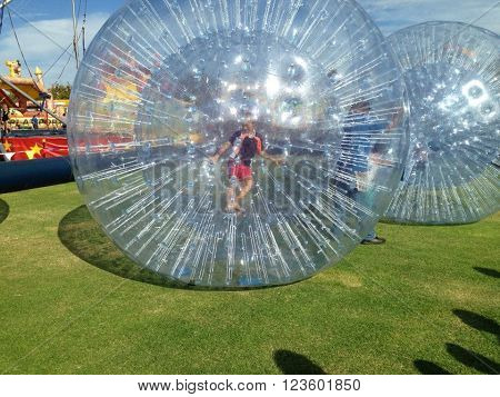 ROCKINGHAM,WA,AUSTRALIA-MAY 12,2014:  Carnival event with people walking inside inflatable large clear balls on a green lawn in Rockingham, Western Australia.