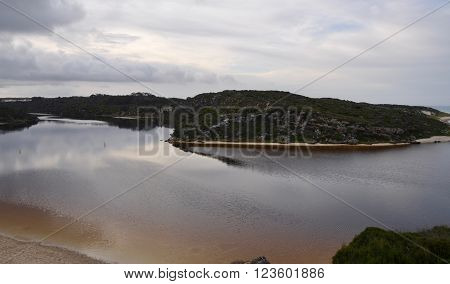 Elevated view over the Moore River, a river mouth in Guilderton, Western Australia, with vegetated coastal dunes under an overcast sky at dawn.