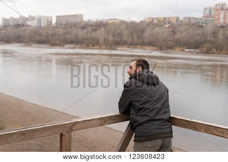 Bored man leaning his  elbows on railing and looking at the river