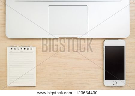 Top view of office desk with small notebook mobile phone and laptop on wooded table