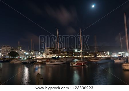 Long exposure city lights across bay boats in foreground blurred while gently rocking and city buildings light reflected on water Wellington Harbor New Zealand