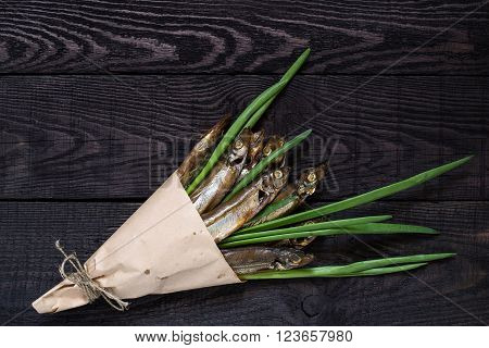 Smoked capelin with green onions in paper cornet on dark wooden background. Top view