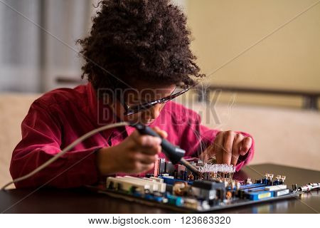 Afro boy soldering motherboard. Darkskinned boy solders motherboard. I know what to do. Very specific hobby.