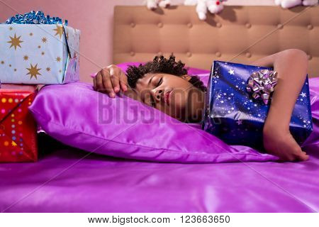 Sleeping child hugs gift box. Sleeping afro boy hugs present. Imagine his joy. This morning will be marvelous.