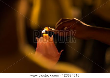 Hand lighting a candle from another candle during a religious ceremony.