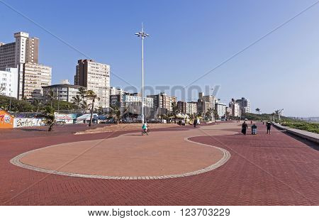 DURBAN SOUTH AFRICA - MARCH 23 2016: Early morning view of many unknown people walking along paved promenade against city skyline in Durban South Africa