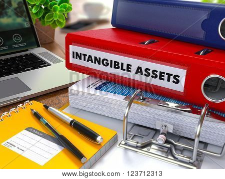 Red Ring Binder with Inscription Intangible Assets on Background of Working Table with Office Supplies, Laptop, Reports. Toned Illustration. Business Concept on Blurred Background. 3D Render.