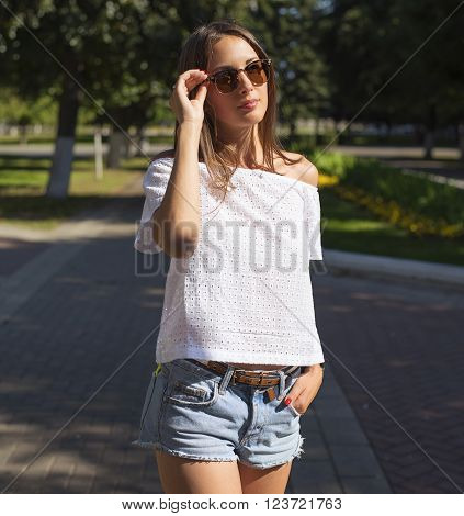 Beautiful girl walking in the city, in a white jacket, sunglasses, shorts, fashion style urban life, a bright sunny summer day. Outdoors woman.