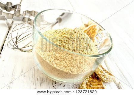 Sesame flour in a glass cupl with a mixer and molds for cookies, sesame seeds, cookies on a wooden boards background